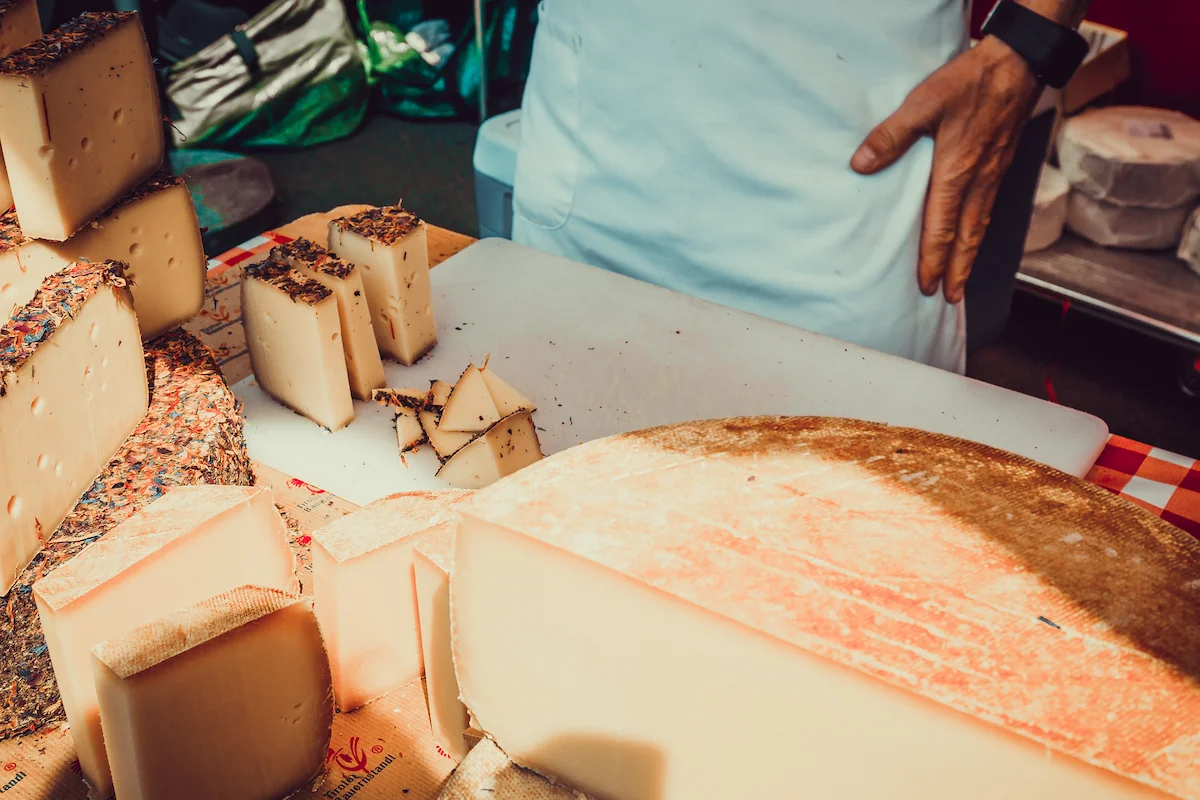 Formaggi stagionati e aromatizzati disposti su un banco da mercato, con fette tagliate su un tagliere e un casaro in grembiule bianco sullo sfondo, simbolo di tradizione e gusto genuino.